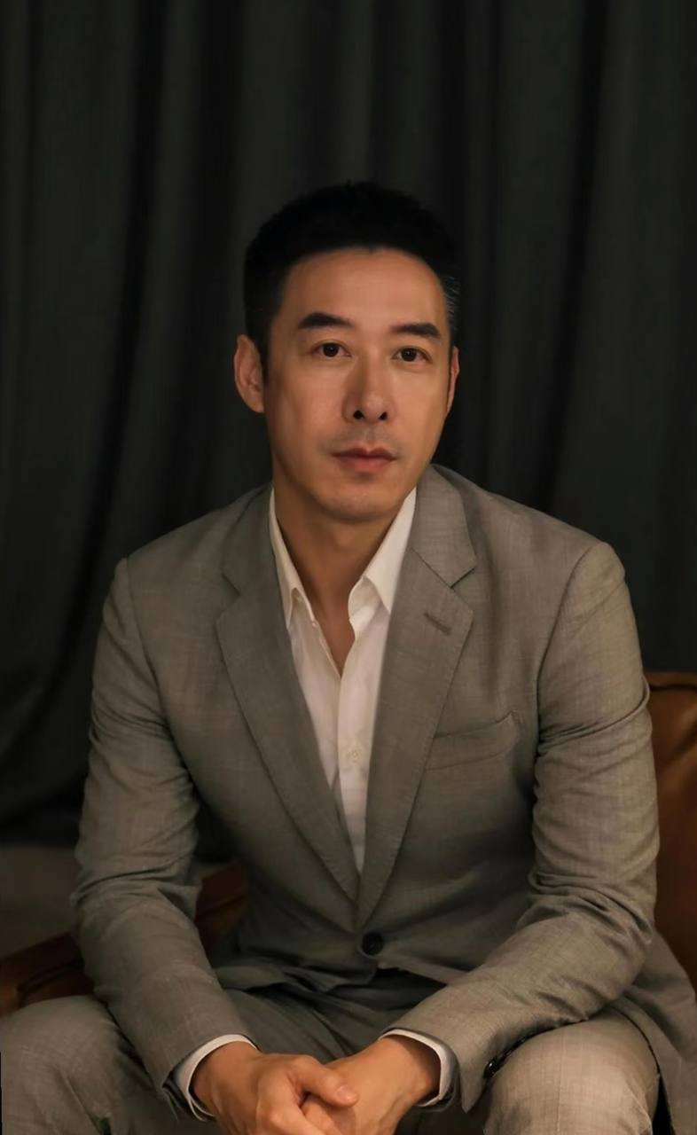 林承睿穿著灰色西裝與白色襯衫，雙手交握坐在深色布幕前的個人形象照。